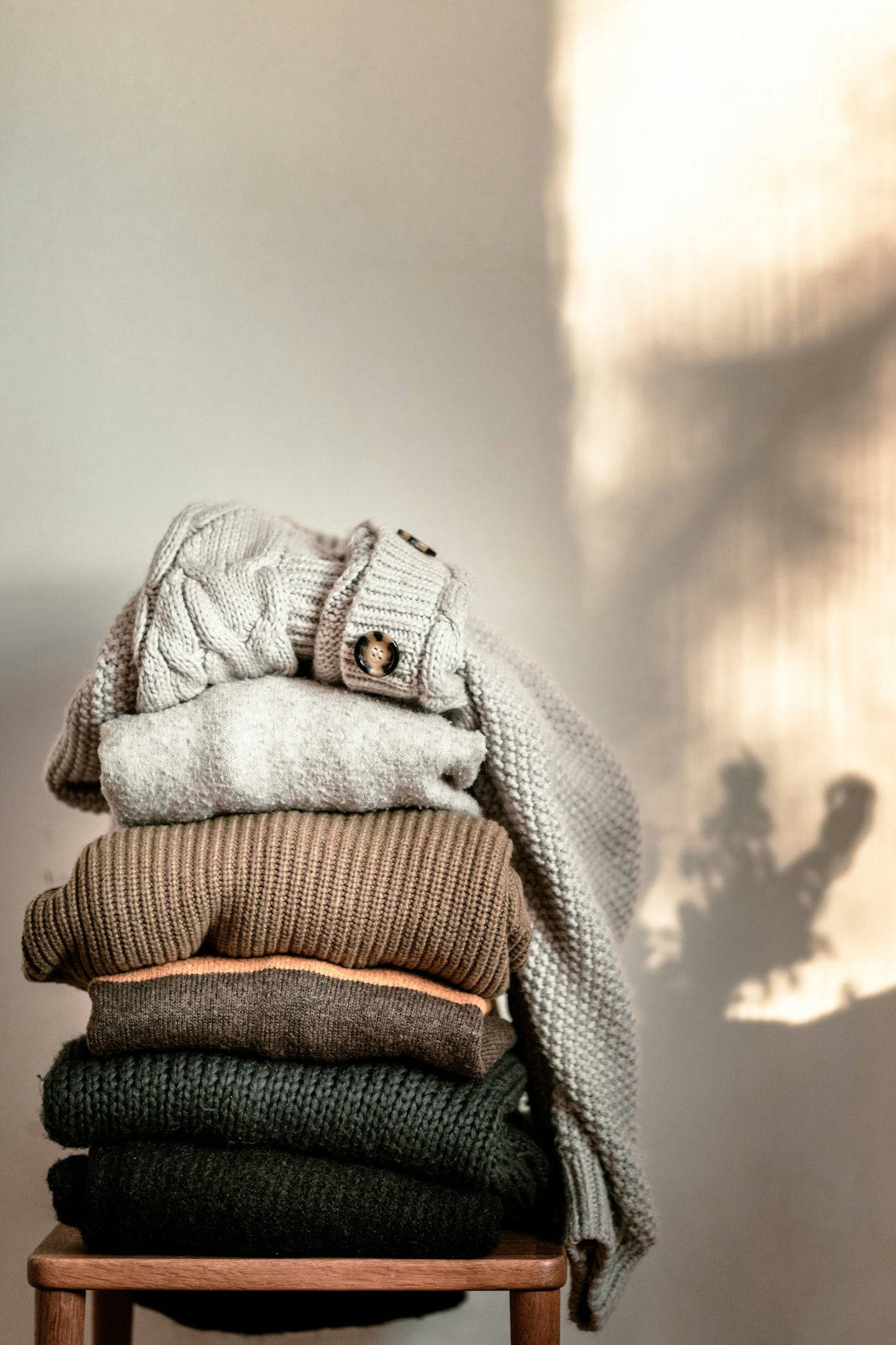 Stack of folded sweaters in natural tones on a wooden chair